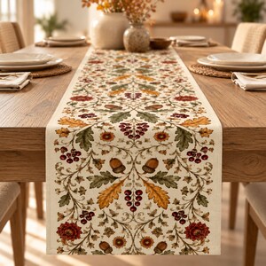May include: A rectangular table runner featuring a cream-coloured background with a repeating botanical pattern of autumn-toned oak leaves, acorns, red berries, and floral motifs in shades of orange, brown, deep red, and muted green.