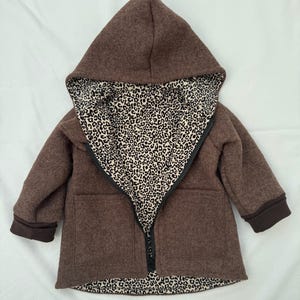 May include: A brown hooded jacket featuring a black zipper closure and a contrasting interior lining with a black and white leopard print pattern. The jacket includes long sleeves with dark brown cuffs and two front pockets on the outer shell.