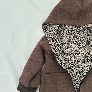 May include: A brown hooded jacket featuring a black zipper closure and a contrasting interior lining with a black and beige leopard print pattern. The garment includes long sleeves with dark brown cuffs and two front pockets on the exterior.