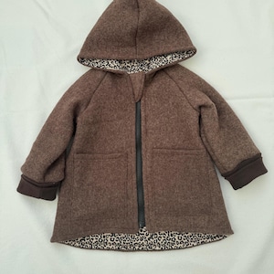 May include: A brown hooded jacket featuring a black front zipper closure, long sleeves with dark brown cuffs, and two front pockets. The interior lining of the hood and the bottom hem of the jacket display a black and white leopard print pattern.