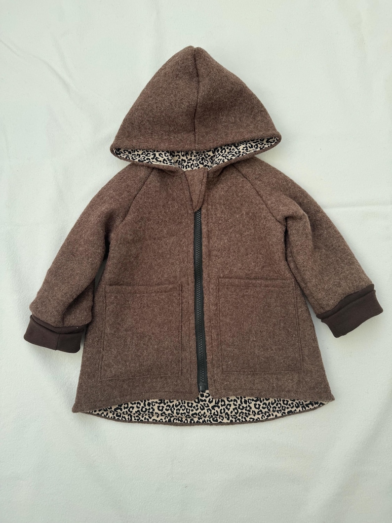 May include: A brown hooded jacket featuring a black front zipper closure, long sleeves with dark brown cuffs, and two front pockets. The interior lining of the hood and the bottom hem of the jacket display a black and white leopard print pattern.