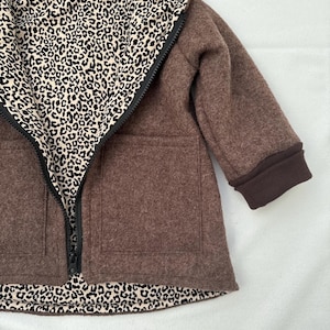 May include: A brown hooded jacket featuring a black zipper closure and two front patch pockets. The interior lining and the inside of the hood display a black and beige leopard print pattern. The sleeves are finished with solid brown ribbed cuffs.
