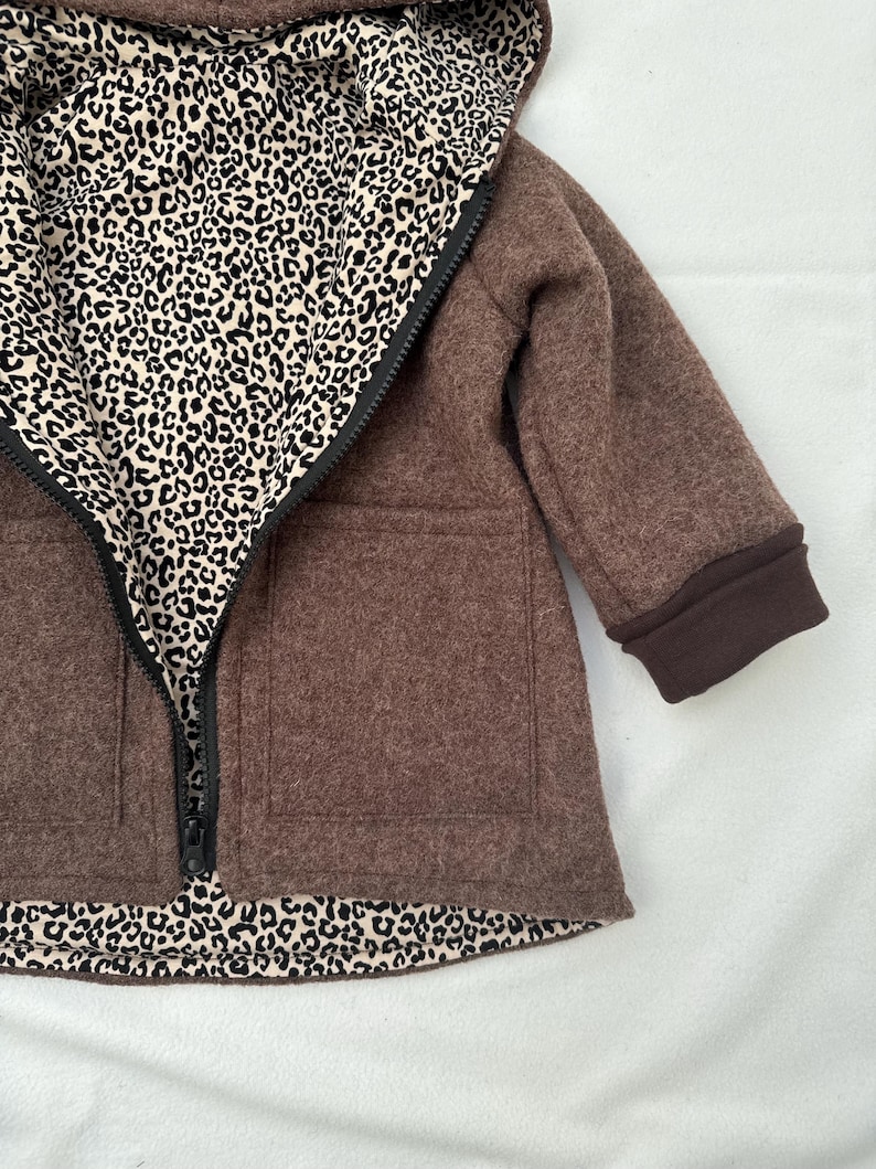 May include: A brown hooded jacket featuring a black zipper closure and two front patch pockets. The interior lining and the inside of the hood display a black and beige leopard print pattern. The sleeves are finished with solid brown ribbed cuffs.