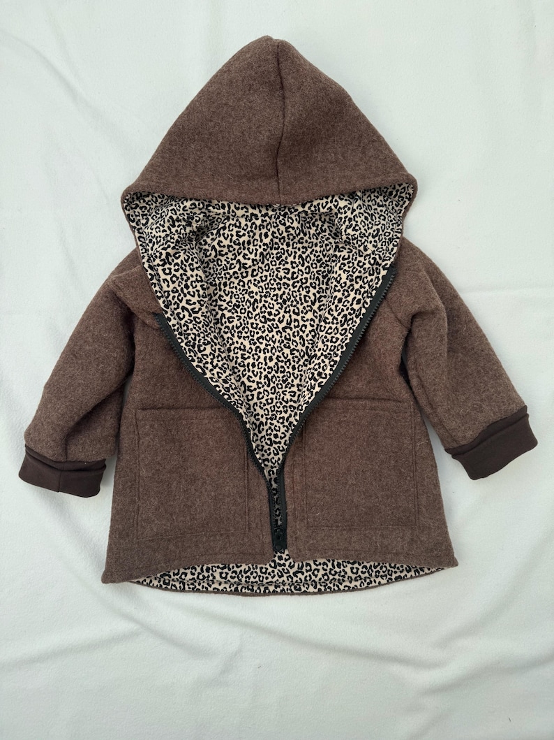 May include: A brown hooded jacket featuring a black zipper closure and a contrasting interior lining with a black and white leopard print pattern. The jacket includes long sleeves with dark brown cuffs and two front pockets on the outer shell.