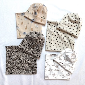 Op de afbeelding: Drie sets van bijpassende mutsen en nekwarmers met diverse patronen, waaronder een beige safari-dierenprint, een crème luipaardprint en een witte achtergrond met zwarte lijntekeningen van oerwouddieren en tropische planten.