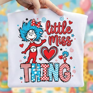 May include: White t-shirt with a cartoon character in a red outfit and blue hair. The words "little miss" are in red script above the word "THING" in a patterned font. Hearts and stars are scattered around the design.
