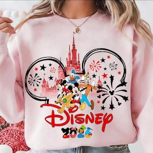 K&ouml;nnte beinhalten: Hellrosa Sweatshirt mit Disney-Design. Das Design zeigt Micky Maus, Minnie Maus, Donald Duck und Goofy vor einem Schloss. Das Wort "Disney" ist rot, darunter steht "2023".