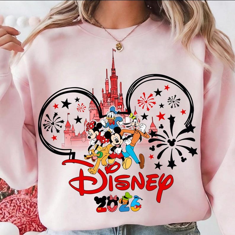 K&ouml;nnte beinhalten: Hellrosa Sweatshirt mit Disney-Design. Das Design zeigt Micky Maus, Minnie Maus, Donald Duck und Goofy vor einem Schloss. Das Wort "Disney" ist rot, darunter steht "2023".