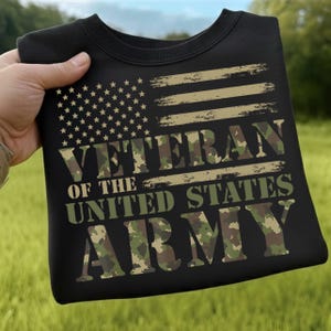 May include: Black sweatshirt featuring a distressed American flag design with the text "VETERAN OF THE UNITED STATES ARMY" in camouflage lettering. The sweatshirt has a crew neck and long sleeves.