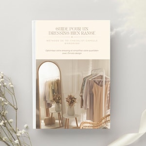 Könnte beinhalten: Ein Buch mit dem Titel "GUIDE POUR UN DRESSING BIEN RANGE" mit französischem Text. Das Cover zeigt einen Spiegel, der Kleidung und eine Kleiderstange reflektiert. Das Buch wirbt für eine Capsule-Wardrobe-Methode zur Organisation eines Ankleidezimmers.