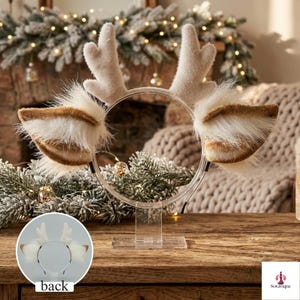May include: A headband featuring two upright, fuzzy, light beige reindeer antlers and two large, fluffy, white and brown faux fur ears extending from the sides. The headband is displayed on a clear acrylic stand, with a small inset showing the back view.