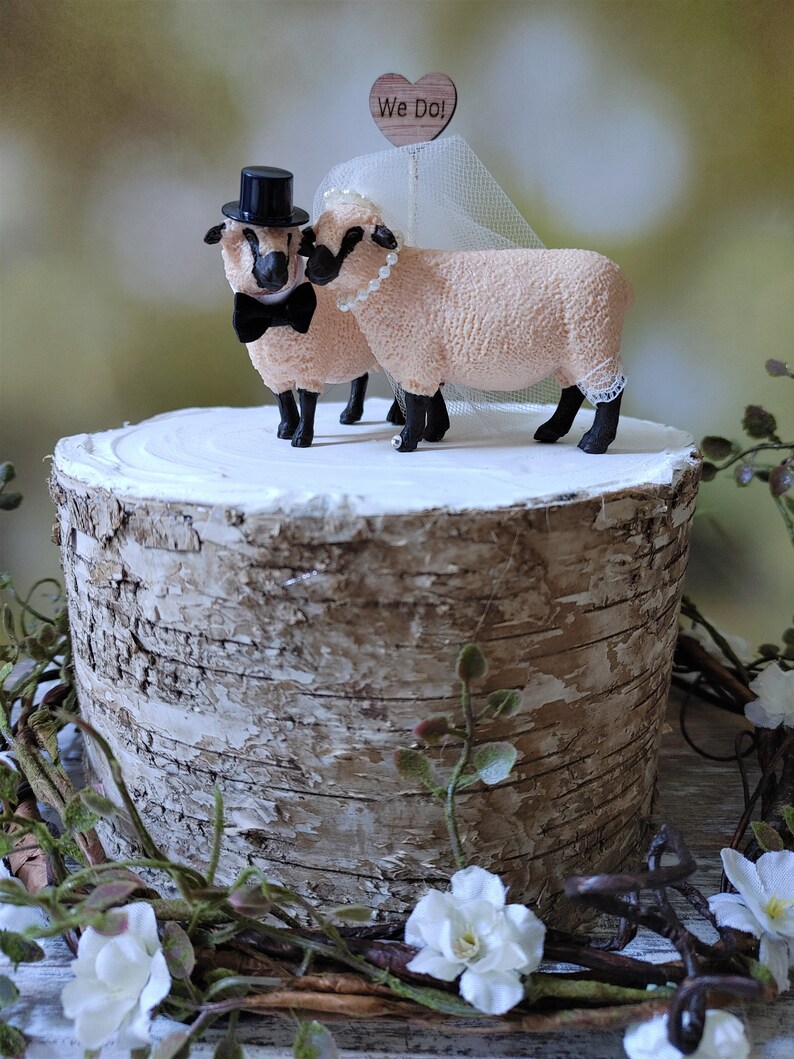 Pu&ograve; includere: Un topper per torta nuziale con una statuina di pecora sposa e sposo. La pecora sposa indossa un velo bianco e una collana di perle. La pecora sposo indossa un cappello a cilindro nero e un papillon nero. Il topper ha un piccolo cartello di legno a forma di cuore che dice "We Do!"