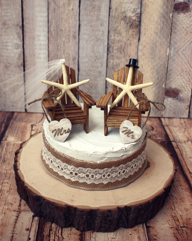 May include: A rustic wedding cake topper featuring two miniature wooden chairs with starfish accents. The chairs are decorated with burlap and lace, and the words "Mr." and "Mrs." are displayed on wooden hearts.