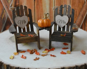 May include: A wedding cake topper featuring two miniature wooden chairs with heart-shaped signs that say "Mr." and "Mrs." A small orange pumpkin sits on a table between the chairs. The chairs and pumpkin are on a wooden slice.
