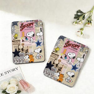 Può includere: Due custodie rettangolari a tema Snoopy. Ogni custodia presenta un design a collage con Snoopy, Charlie Brown e altri personaggi. Le custodie hanno uno sfondo in stile giornale con il testo "Snoopy Stars The Matchmaker". Ogni custodia ha una stella blu scuro.