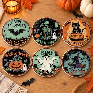 May include: A set of six round drink coasters featuring Halloween-themed illustrations. Designs include a bat, a skeleton with the text 'KEEP IT GREEN', a cat on a pumpkin with 'DON'T BE A SCAREDY CAT', a jack-o'-lantern, a ghost with 'BOO', and a witch.