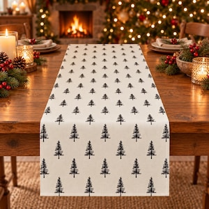 May include: A rectangular table runner featuring a repeating pattern of black pine tree silhouettes printed on a cream-colored fabric. The runner is laid flat across a wooden dining table, showcasing a consistent grid of trees.