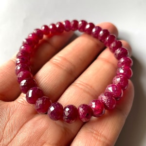 May include: A circular bracelet composed of numerous small, faceted, deep red gemstone beads. Each bead features a multi-faceted surface that reflects light, creating a sparkling appearance throughout the continuous, elasticized string of dark crimson stones.