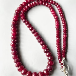 May include: A necklace composed of numerous small, faceted, deep red gemstone beads arranged in a single strand. The beads gradually increase in size towards the centre. A silver-toned metal hook clasp is attached to one end of the necklace.