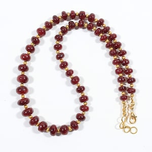 May include: A necklace featuring a repeating pattern of deep red, rounded, translucent beads interspersed with small, spherical, metallic gold-toned spacers. The strand concludes with a gold-toned lobster claw clasp and a short extender chain.