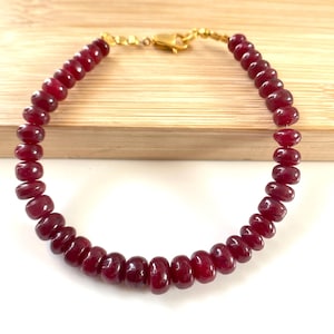 May include: A bracelet composed of numerous small, round, deep red beads strung together. The piece features a gold-toned metal lobster claw clasp and small gold-toned spacer beads at the ends near the closure mechanism.