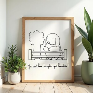 Può includere: Una stampa artistica incorniciata con un disegno a linee bianche e nere di un coniglio dietro una staccionata accanto a un albero. Sotto l'illustrazione, il testo recita: "You don't have to explain your boundaries." La cornice è in legno chiaro.