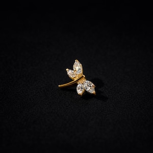May include: A gold-colored dragonfly-shaped stud earring with clear, sparkling gemstones. The earring features a delicate design with three gemstones on each wing and a single gemstone on the body, set against a black background.