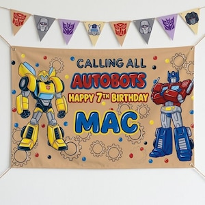 Peut inclure: Une bannière d'anniversaire beige avec Bumblebee et Optimus Prime, portant le texte "CALLING ALL AUTOBOTS HAPPY 7TH BIRTHDAY MAC" en bleu et rouge. Au-dessus, une guirlande de fanions triangulaires affiche diverses icônes de robots.