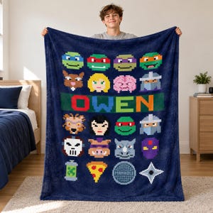 May include: A dark blue plush throw blanket featuring a pixelated grid of various cartoon character faces and icons, including a slice of pizza and a manhole cover. The name OWEN is printed in large, colourful pixelated letters across the centre.