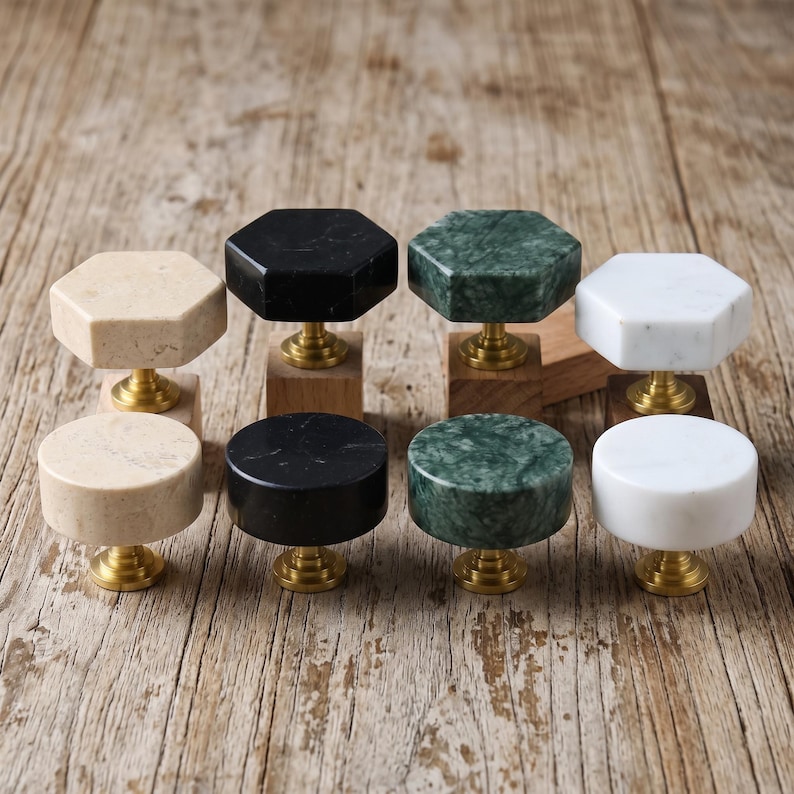 May include: A collection of eight cabinet knobs featuring smooth stone tops in beige, black, green, and white. Four knobs have a hexagonal shape and four have a circular shape. Each knob is attached to a polished brass base and a small wooden block.