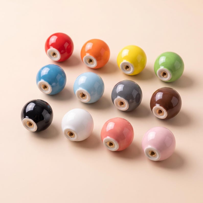 Puede incluir: Una colecci&oacute;n de once pomos esf&eacute;ricos de cer&aacute;mica para armarios en varios colores s&oacute;lidos, incluyendo rojo, naranja, amarillo, verde, azul, azul claro, gris, marr&oacute;n, negro, blanco, coral y rosa, cada uno con un inserto met&aacute;lico roscado central.