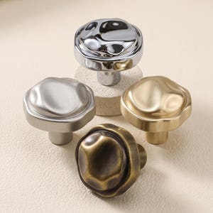 May include: Four cabinet knobs with irregular, organic, rounded tops. The set includes one polished chrome knob, one matte silver knob, one brushed gold knob, and one dark antique bronze knob, each featuring a central mounting post.