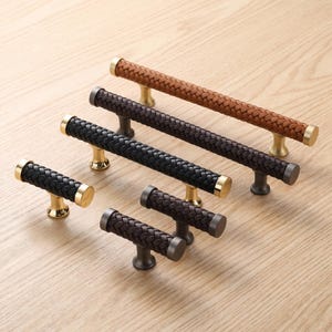 May include: A collection of five cabinet pulls and knobs featuring a braided leather texture. The set includes one long tan pull, one long black pull, one medium black pull, and two small dark brown knobs, all with metallic end caps and bases.
