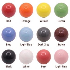 Puede incluir: Una colecci&oacute;n de doce pomos esf&eacute;ricos dispuestos en una cuadr&iacute;cula, cada uno con un acabado brillante s&oacute;lido. Los colores incluyen rojo, naranja, amarillo, verde, azul, azul claro, gris oscuro, marr&oacute;n, negro, blanco, rosa y rosa claro, con etiquetas.