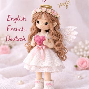 Può includere: Una bambola angelo all'uncinetto con lunghi capelli castani, un'aureola floreale e ali bianche. La bambola indossa un vestito bianco e tiene in mano un cuore rosa. L'immagine include il testo "crochet pattern pdf" e le parole "English, French, Deutsch".