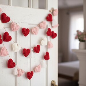 Peut inclure: Une guirlande de c&oelig;urs faite &agrave; la main, rouge, rose et blanche, est suspendue &agrave; une porte blanche. Les c&oelig;urs crochet&eacute;s sont enfil&eacute;s sur de la ficelle naturelle, cr&eacute;ant une d&eacute;coration charmante et festive. Parfait pour la Saint-Valentin.