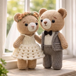 May include: Two crocheted teddy bears, a bride and groom, stand side-by-side. The bride bear wears a white dress, veil, and floral crown. The groom bear is dressed in a gray suit with a black bow tie. The bears are tan with white and pink accents.