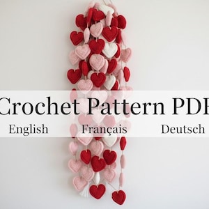 Peut inclure: Une guirlande de c&oelig;urs crochet&eacute;s rouges, roses et blancs. Les c&oelig;urs sont enfil&eacute;s ensemble, cr&eacute;ant un ornement d&eacute;coratif. Le texte sur l'image indique "Crochet Pattern PDF" avec "English", "Fran&ccedil;ais" et "Deutsch" en dessous.