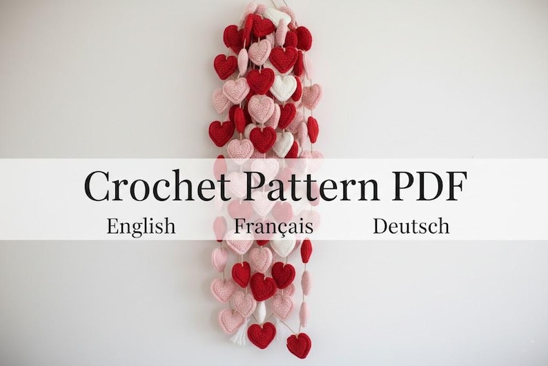 Peut inclure: Une guirlande de c&oelig;urs crochet&eacute;s rouges, roses et blancs. Les c&oelig;urs sont enfil&eacute;s ensemble, cr&eacute;ant un ornement d&eacute;coratif. Le texte sur l'image indique "Crochet Pattern PDF" avec "English", "Fran&ccedil;ais" et "Deutsch" en dessous.