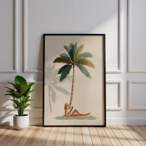 May include: Framed art print featuring a person relaxing under a palm tree, reading a book. The artwork has a vintage aesthetic with a beige background, a black frame, and a potted plant in the foreground. The palm tree has green and yellow fronds.