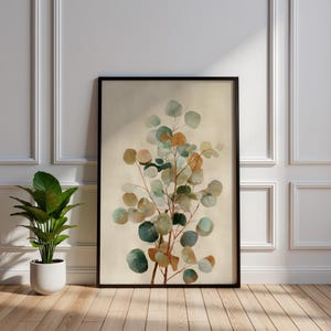May include: A framed botanical print featuring a watercolor illustration of eucalyptus branches with round, multi-toned leaves in shades of green, gold, and brown. The artwork is set against a neutral background and framed in black.