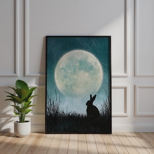 May include: A rectangular framed wall art print featuring a dark silhouette of a rabbit sitting in tall grass against a large, luminous full moon in a starry, deep teal night sky. The artwork is displayed in a thin black frame.
