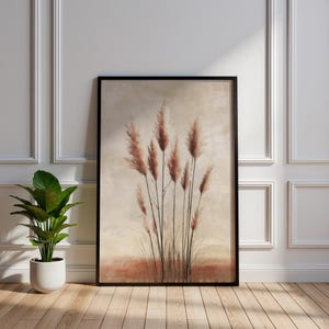 May include: A framed art print depicting pampas grass in a watercolour style. The artwork features shades of brown and beige, set against a neutral background, and is enclosed in a black frame. The artwork is displayed on a wooden floor.