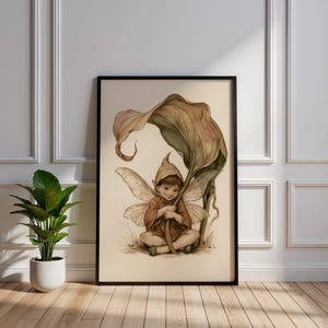Op de afbeelding: Een ingelijste wandkunstprint met een aquarelillustratie van een kleine, gevleugelde figuur met een puntmuts, zittend onder een groot, gebogen blad. De figuur heeft delicate, doorschijnende vleugels en is afgebeeld in zachte, aardse tinten.