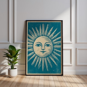 May include: Framed art print featuring a vintage illustration of a smiling sun with radiating beams. The sun is depicted in cream against a teal background, framed in black. The artwork is displayed against a white wall and wooden floor.