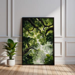 Pode incluir: Uma impressão artística emoldurada que retrata um dossel florestal verde visto de baixo. A obra de arte apresenta folhagem verde exuberante e galhos de árvores contra um céu brilhante e difuso. A impressão está em uma moldura preta, exibida em um piso de madeira ao lado de uma planta em vaso.