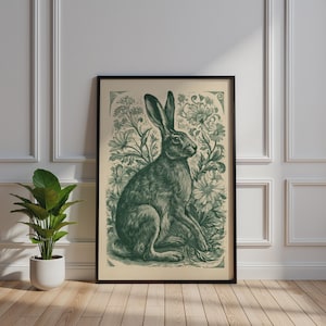 May include: A framed wall art print featuring a dark green illustration of a hare sitting among detailed flowers and foliage on a light cream background. The artwork is enclosed in a thin black frame, showcasing a botanical and animal theme.