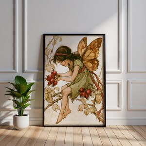 May include: A framed wall art print featuring an illustration of a fairy with large brown wings, wearing a green dress, sitting on a thorny branch and holding a cluster of red berries. The artwork has a muted color palette with earthy tones.
