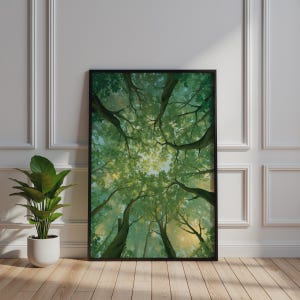 May include: A rectangular wall art print in a black frame featuring a low-angle view of a forest canopy. The image displays tall tree trunks reaching upward with dense green leaves and branches filtering soft sunlight against a pale sky.