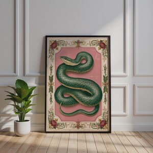 Könnte beinhalten: Ein rechteckiger Wandkunstdruck mit einer gewundenen grünen Schlange, die auf einem altrosa Hintergrund zentriert ist. Die Illustration ist von einem dekorativen cremefarbenen Rand umgeben, der mit komplexen Blumenmotiven und roten Blütenakzenten verziert ist.